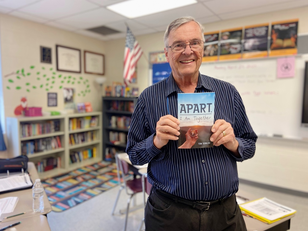 Tom Donlon holding a copy of his book in a JCS classroom