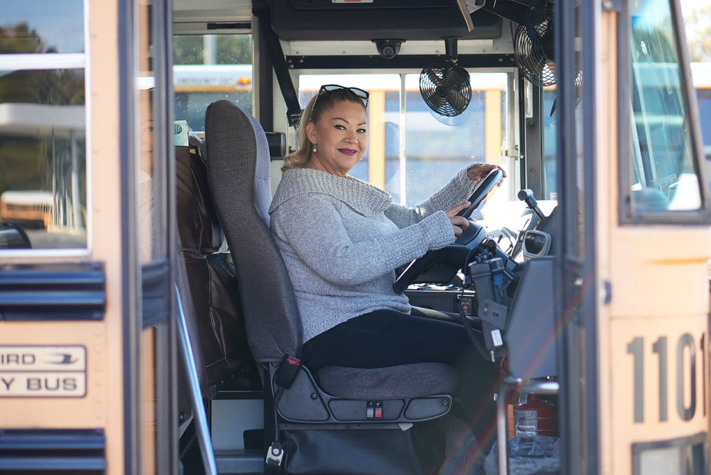 JCS bus operator in driver's seat looking out of bus doors with welcoming smile