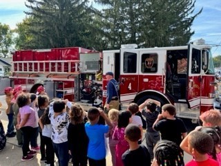 Students listening to a firefighter talk in front of a fire truck